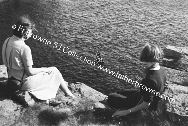 WOMEN SITING ON TOP OF CLIFFS LOOKING AT CURRAGH